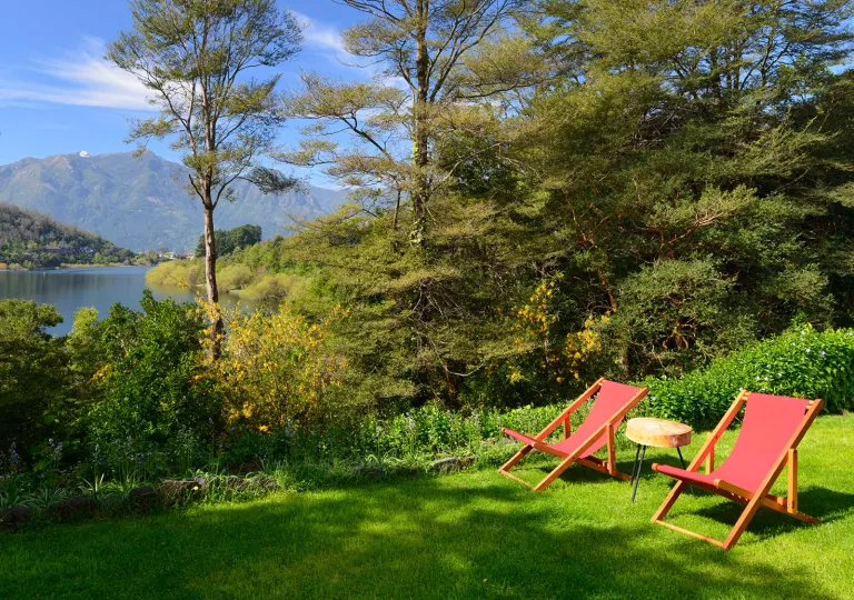 Two red chairs on a field of grass, looking out towards a lake surrounded by trees