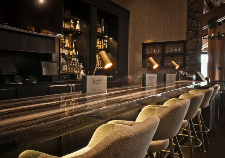 Dimly lit bar with cushioned stools and alcohol on the shelves in the back