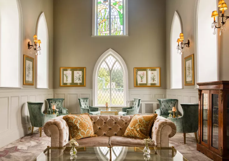 Lounge with cushioned green and red sofas and large, stained glass windows in the background