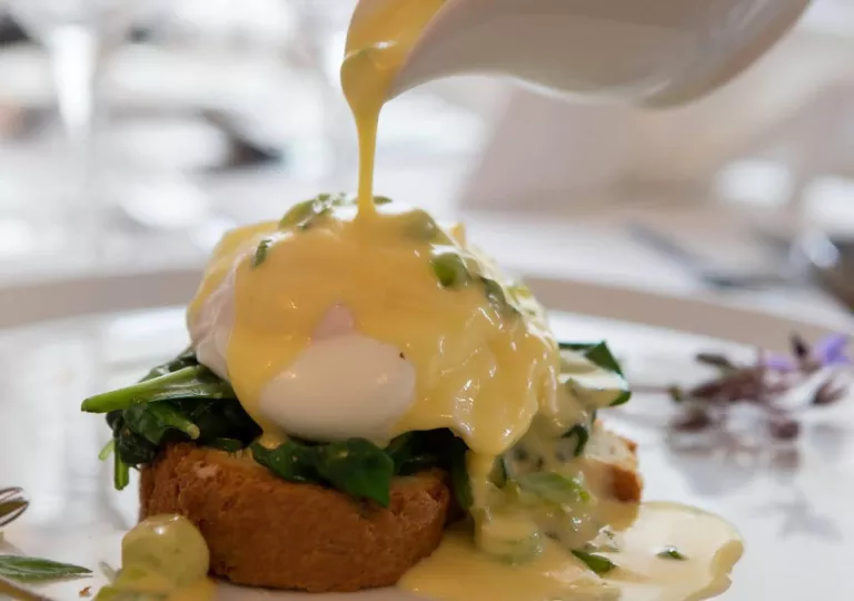 Plate of eggs benedict, while pouring sauce over