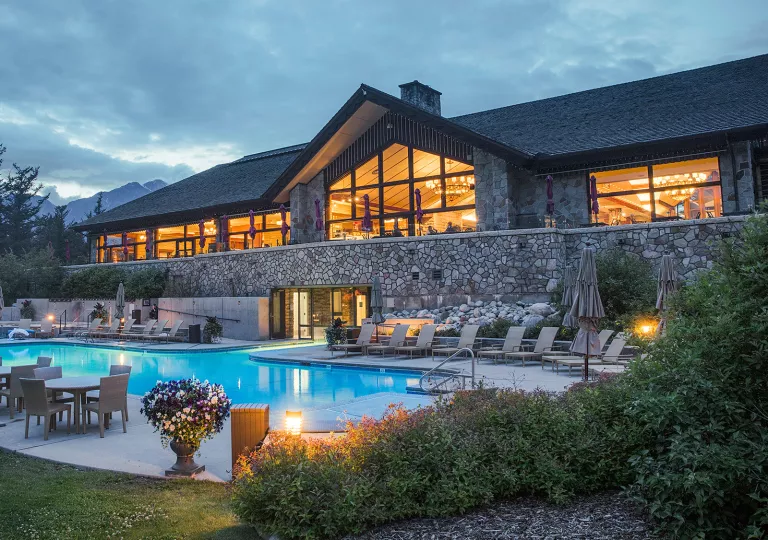 Illuminated hotel building with a stone barricade and outdoor pool in front