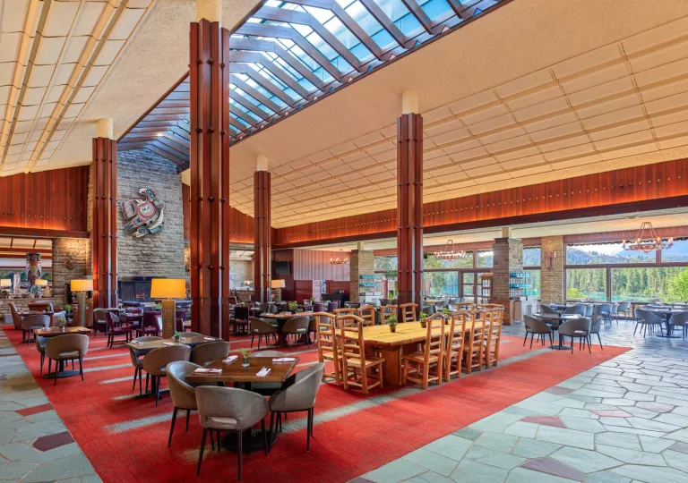 Large restaurant dining hall with red carpet and wooden dining tables, and large wooden pillars