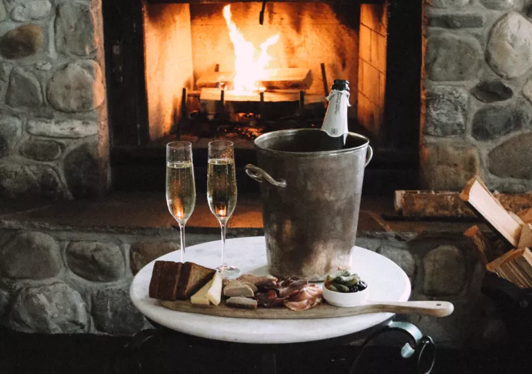 Bucket with a champagne bottle and two glasses to the left, in front of a stone fireplace