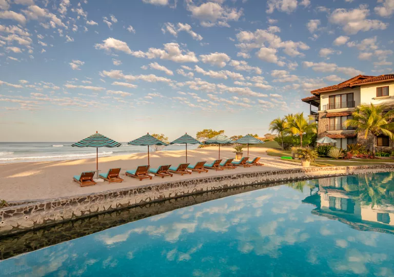 Outdoor pool with a row of reclining chairs looking out to the beach