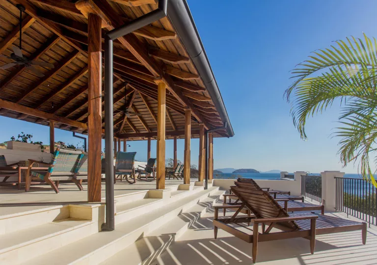 Outdoor patio with wooden roofing and chairs, looking out to the ocean