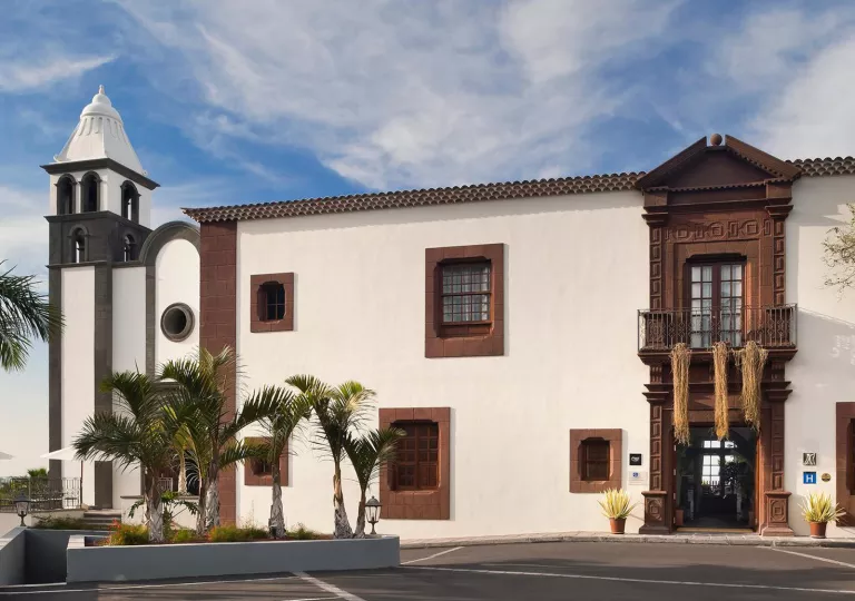 Exterior view of white and brown building, with a bell tower to the left