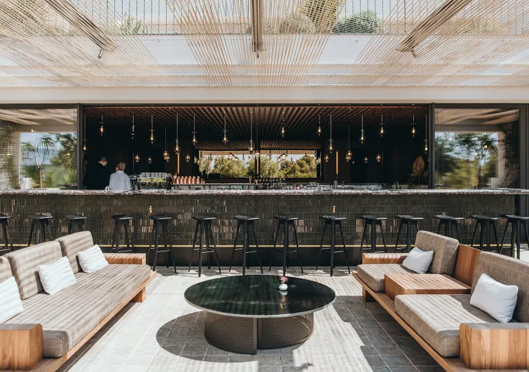 Outdoor patio with cushioned chairs and a large bar counter in the background