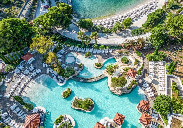 Sky view of outdoor pool surrounded by reclining chairs and the beach in the back