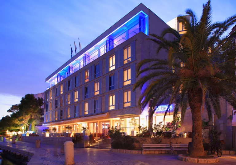 Exterior, evening view of multi-level hotel building with blue and purple illuminated lights