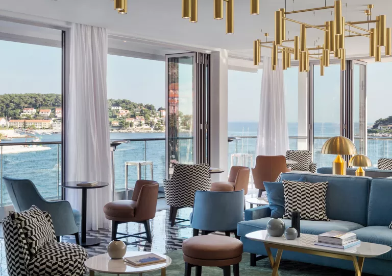 Corner room with cushioned white and blue chairs and large windows looking out towards the ocean