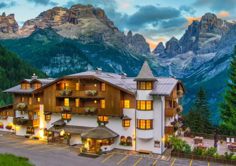Exterior of white and brown hotel building, with large mountains in the background