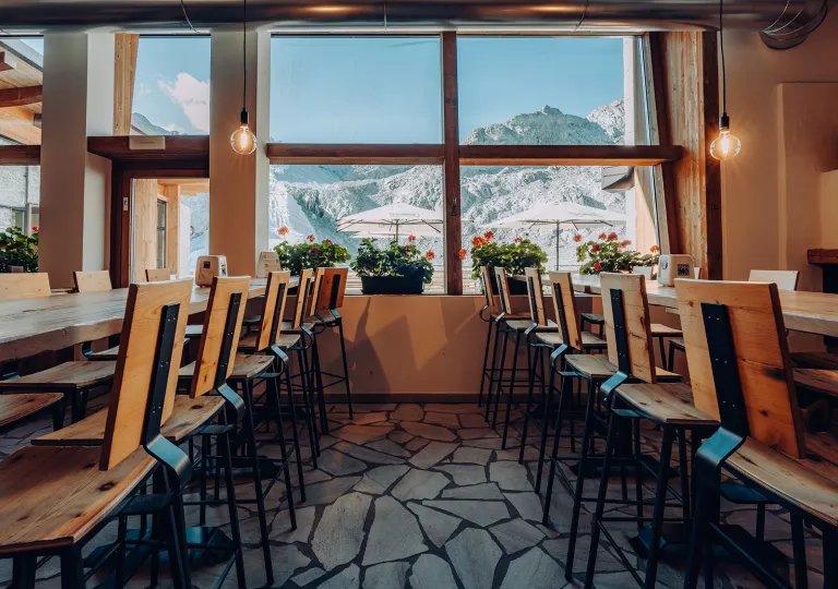 Restaurant dining hall with long tables leading to a window with potted flowers