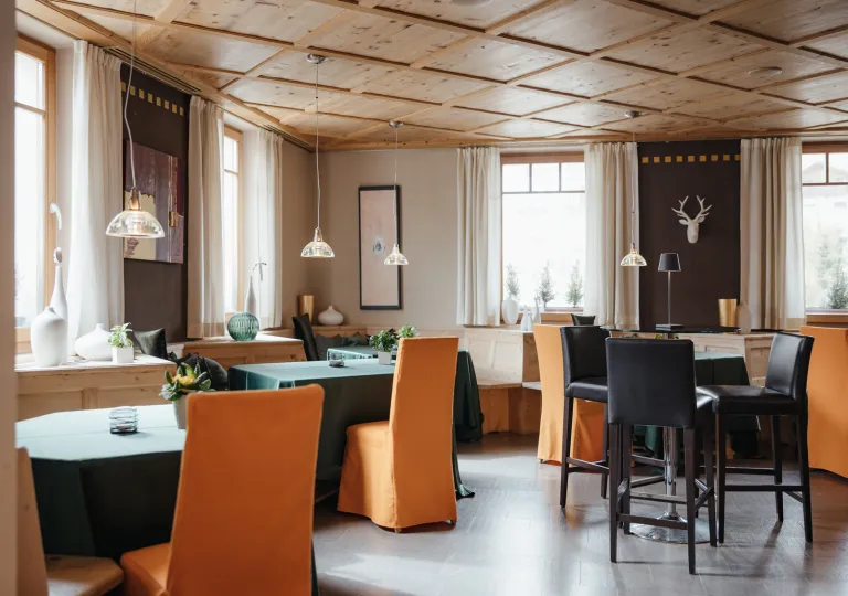 Restaurant dining hall with orange chairs and green dining tables, with art pieces on the walls