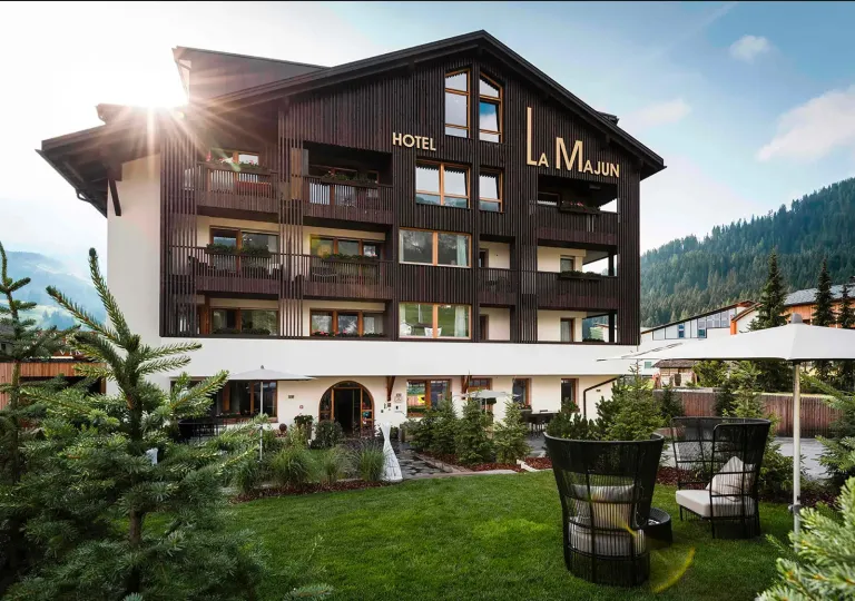 Exterior view of dark brown and white hotel building, with a small grass field in front