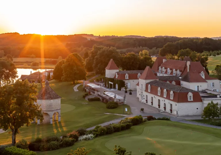 Sky, exterior view of white and red hotel complex, with large grass fields in front