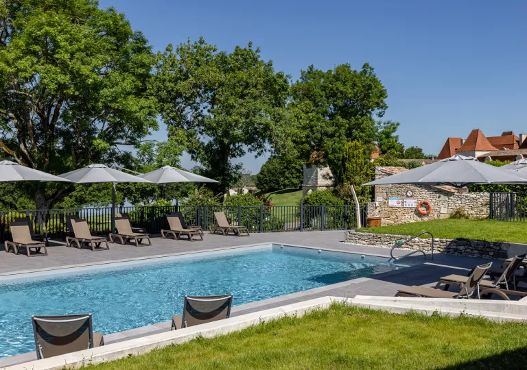 Outdoor pool surrouonded by umbrellas and reclining chairs, with a large lake in the background