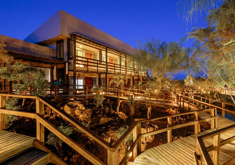 Exterior view of illuminated hotel building with wooden bridges in front