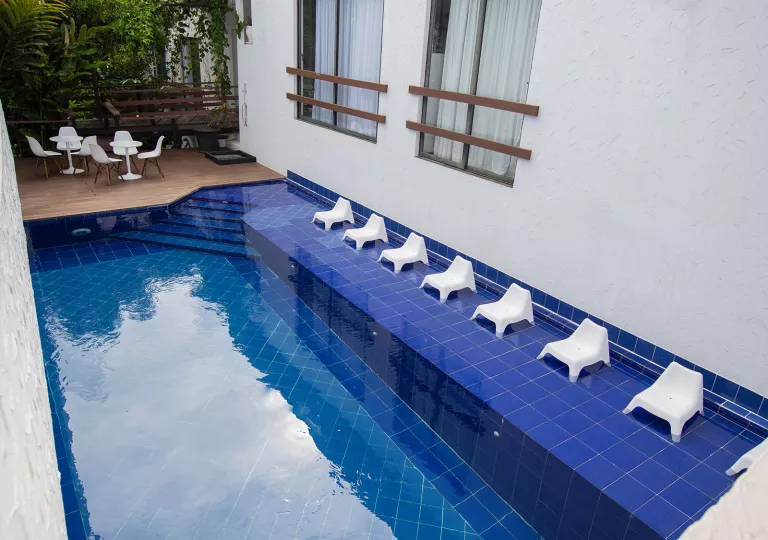 Outdoor blue pool, surrounded by white chairs and a white building to the right