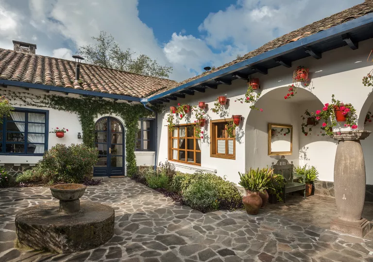 Exterior view of white building with a small fountain and stone flooring in front