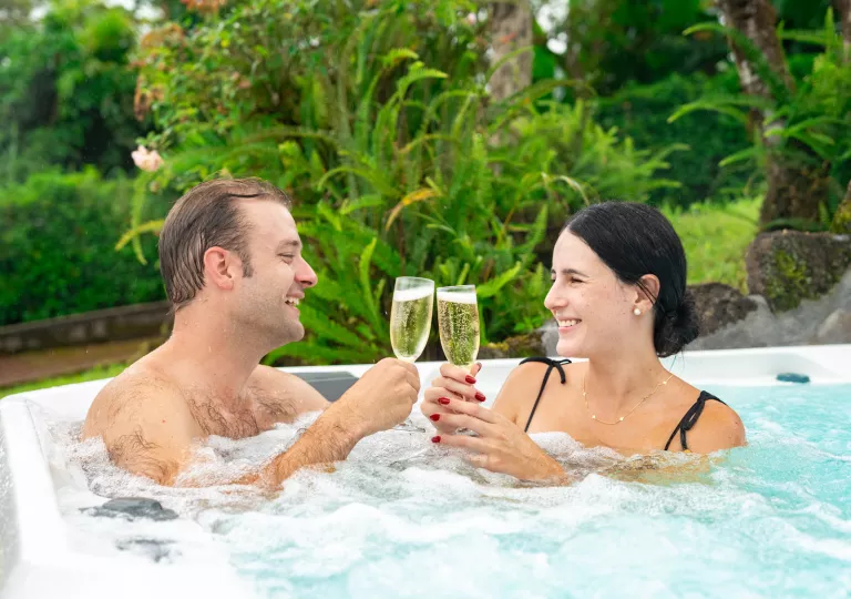Man and woman sitting in a hot tub, clinking their glasses of champagne