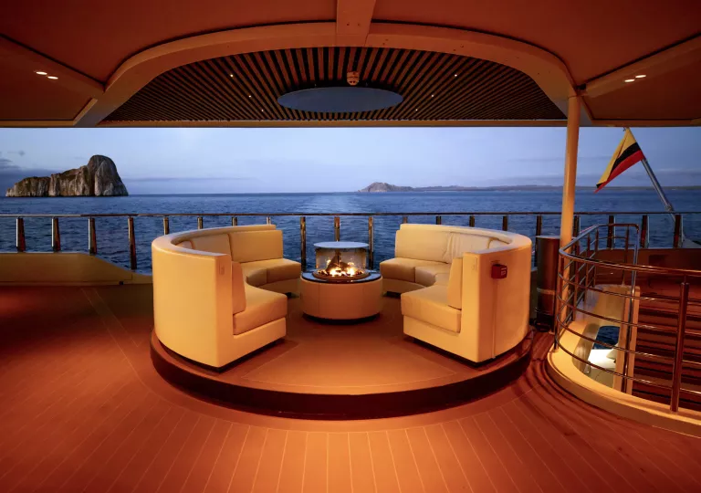 Cruise ship interior with circular sofas surrounding a fire pit, looking out to the ocean