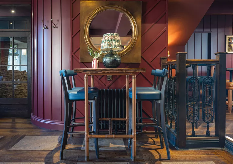 Dining table with a copper tables and blue stools, with a large mirror hanging on the wall