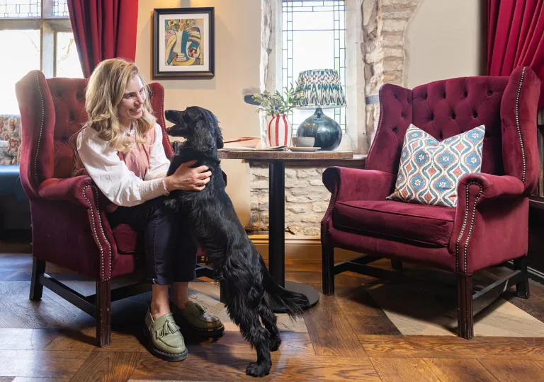 Woman sitting on a red, cushioned chair while playing with a black dog