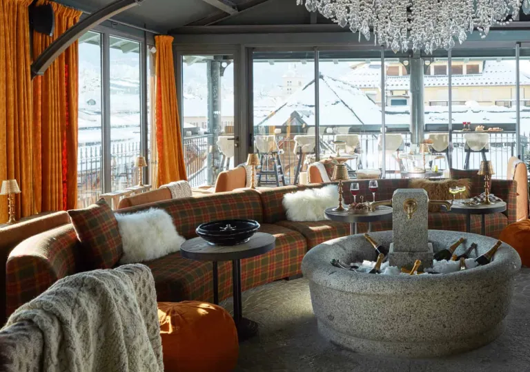 Open room with large windows and a plaid, circular couch, with a large stone fountain with bottles of champagne