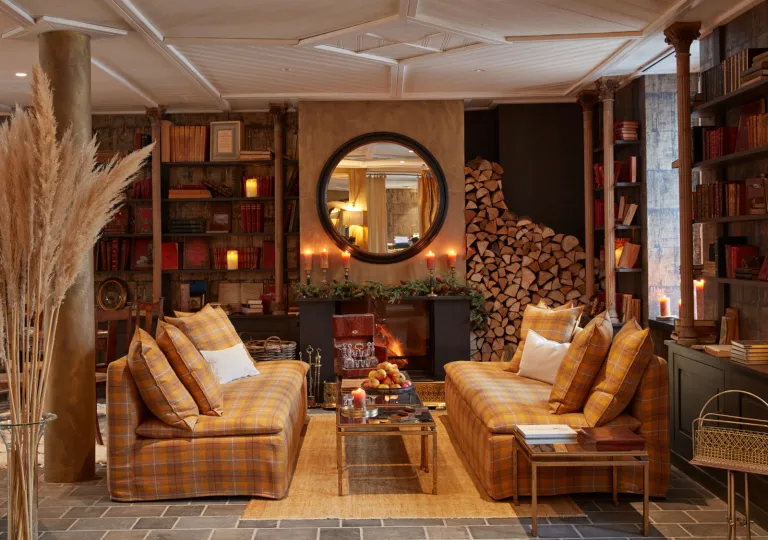 Room with a large fireplace with a giant mirror on top, with two brown, plaid couches in front