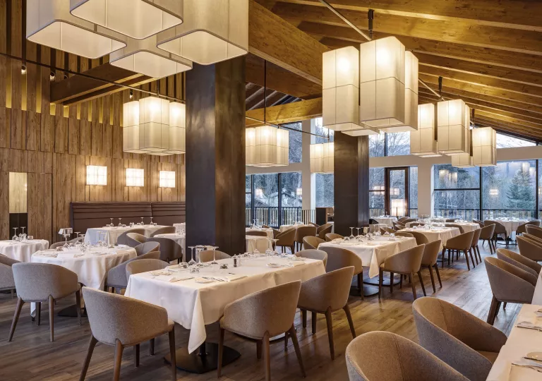 Indoor restaurant dining area with long tables with white table cloths, with cushioned gray chairs surrounding
