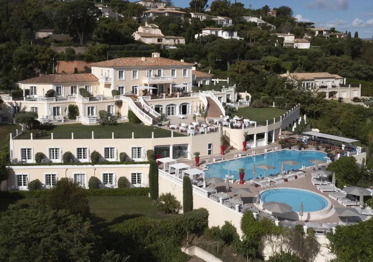Sky, exterior view of white hotel building with an outdoor pool, surrounded by trees