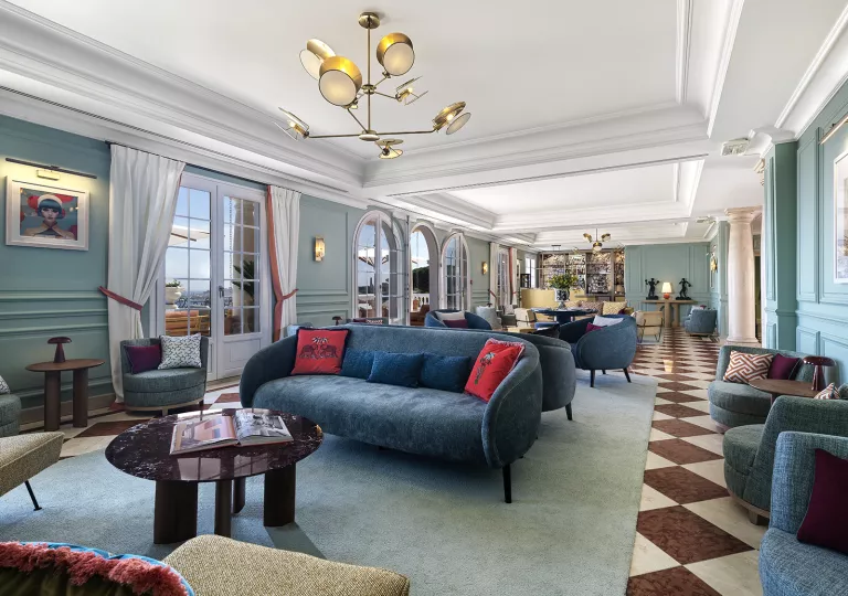 Long room with blue, cushioned sofas with large doors leading to a patio