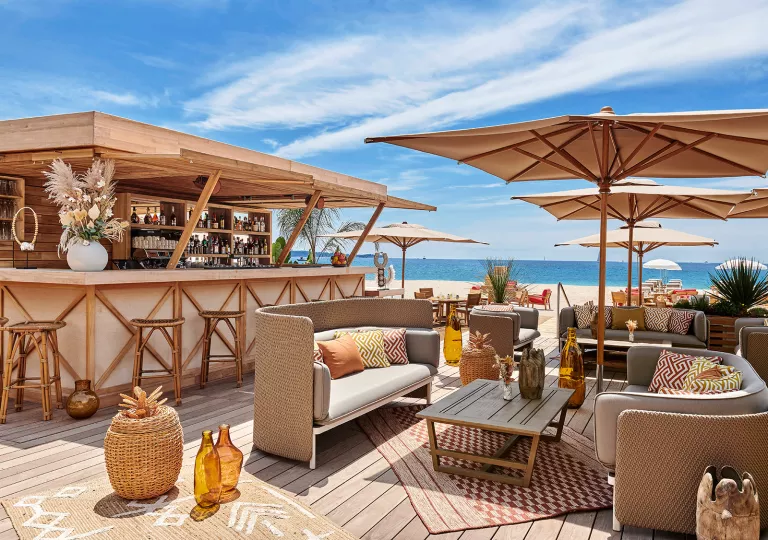 Outdoor bar and patio, with woven chairs and cushions sofas, next to the beach