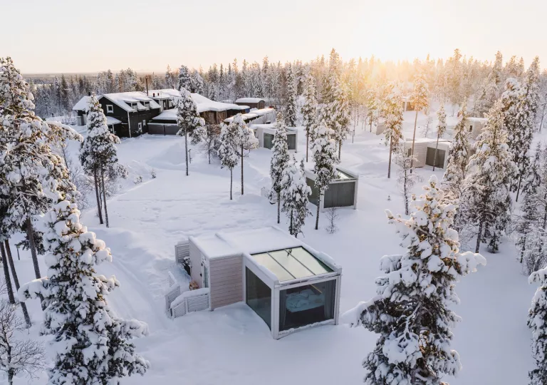 Small glass rooms across a field of snow, with a larger building in the background