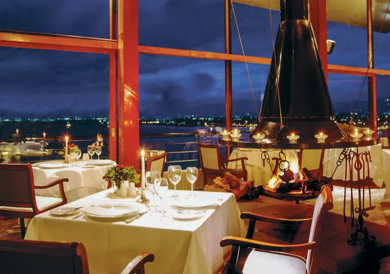 Restaurant dining area with white dining tables and wine glasses on each table, with large glass walls