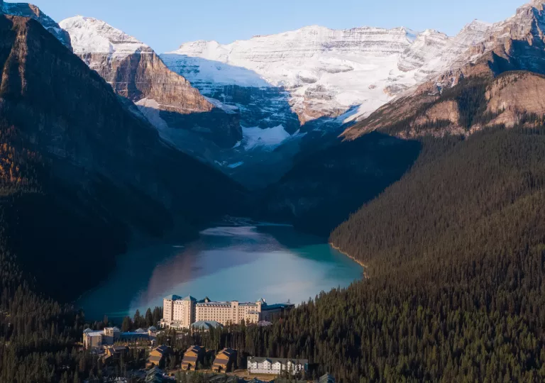 Large valley of trees, with a lake in the center and snow-capped mountains in the background