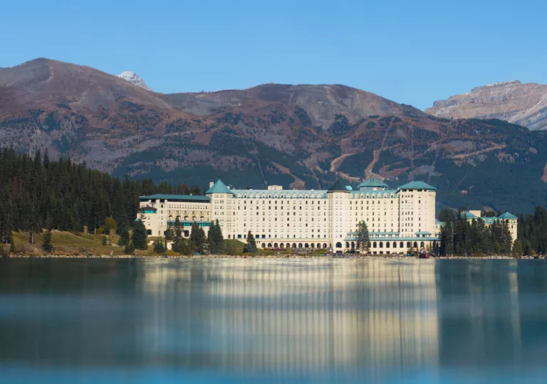 Large exterior view of a white and blue hotel building in front of a large lake