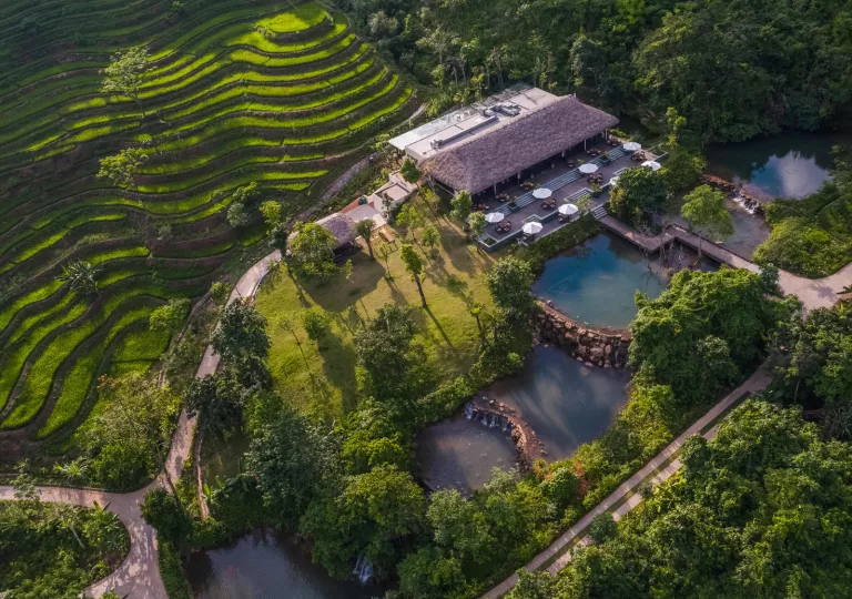 Exterior view of hotel building with outdoor pools, surrounded by trees and plants