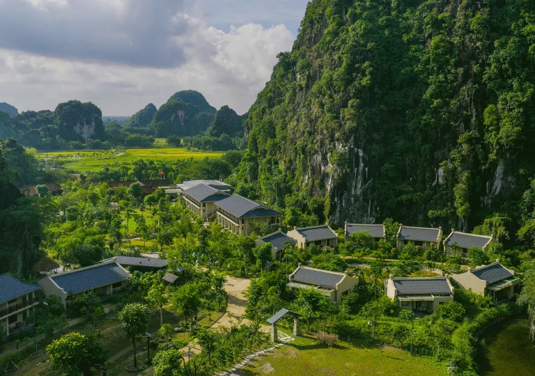 Multiple white buildings surrounded by thick forest and tall mountains
