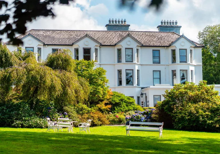 Exterior view of white building with large trees and a grass field in front