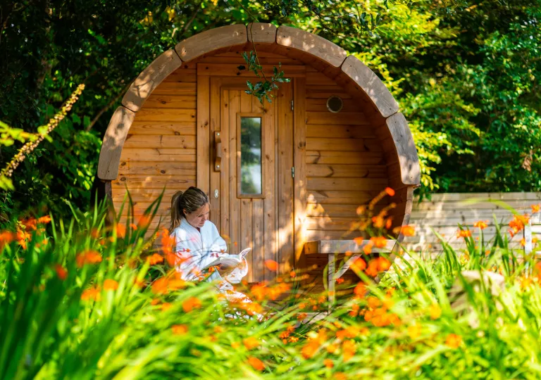 Woman sitting in front of a wooden cabin building, reading a book