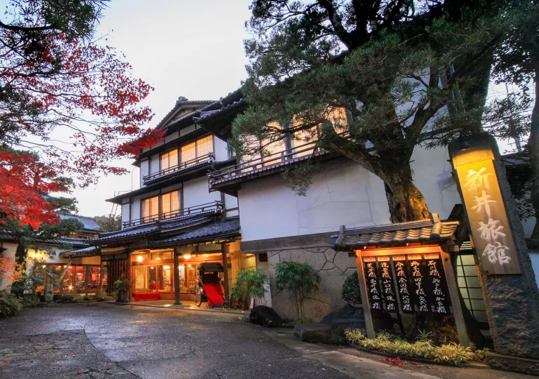 Exterior view of Japanese-style building with large trees and illuminated room