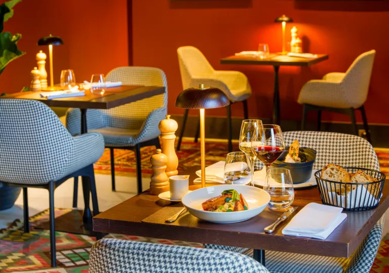 Dining area with checkered chairs, and wooden square tables with plates of food on top