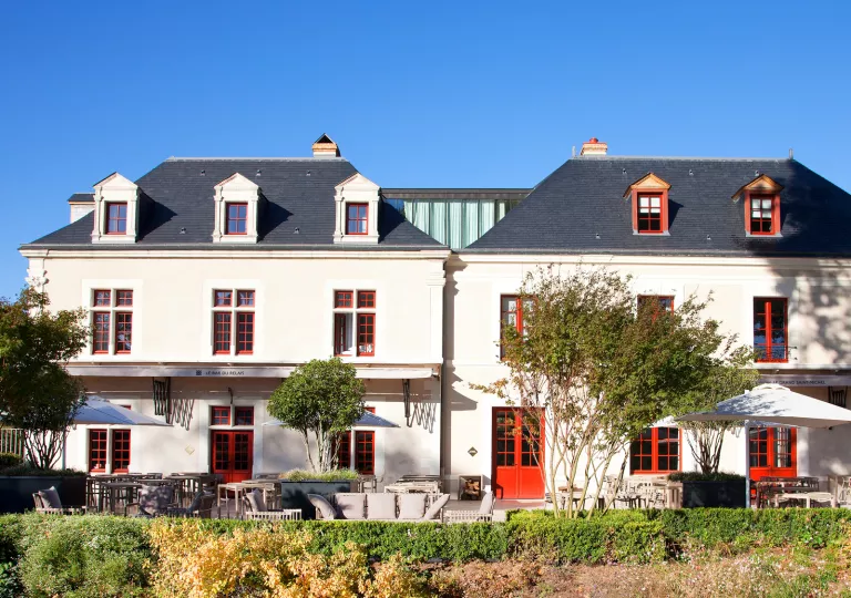 Exterior view of white building with red doors and windows, with small trees in front