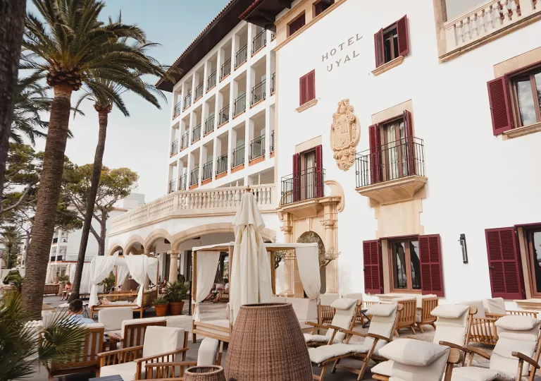 Exterior view of white hotel with large balconies and reclining chairs outside
