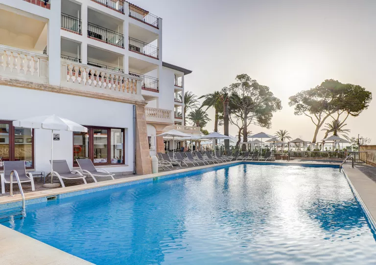 Exterior view of white hotel building with an outdoor pool and the sunset in the background