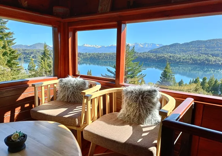Two chairs with fuzzy pillows next to a large window, overlooking a lake