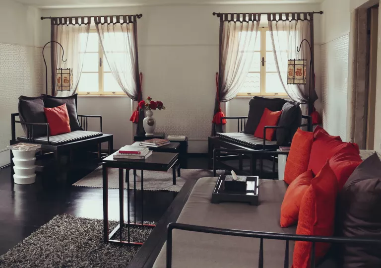 Three wooden chairs with pillows and cushions in a room with black floors and long curtains on the windows