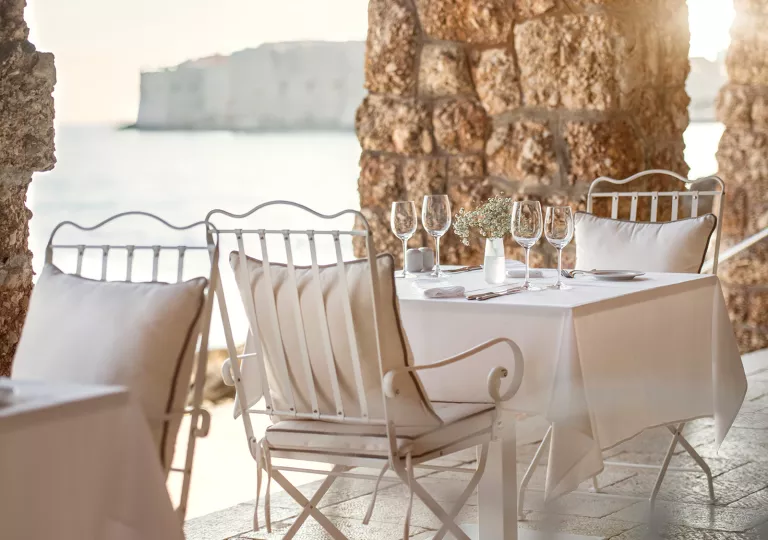 Outdoor patio with large stone pillars and white dining tables with wine glasses