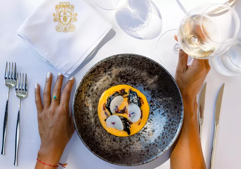 Dark gray bowl with an orange puree and vegetables, with a glass of wine to the right